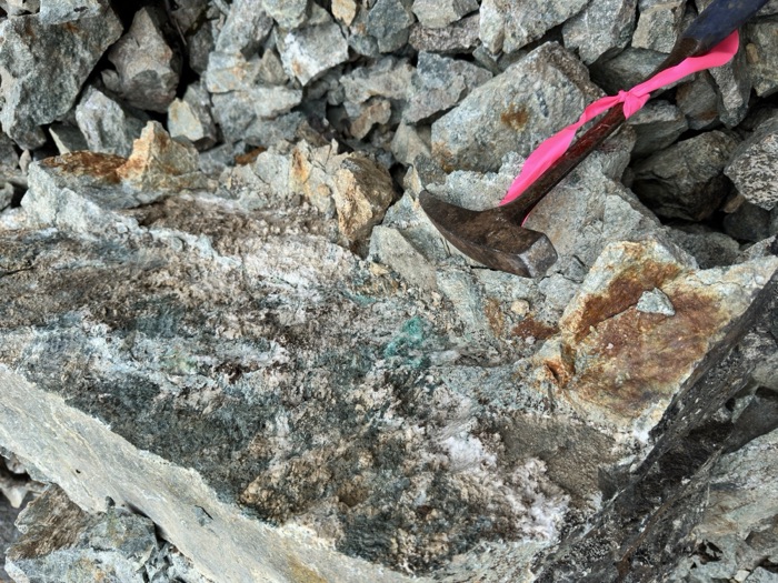 Copper mineralization in outcrop — rock hammer and flagging tape