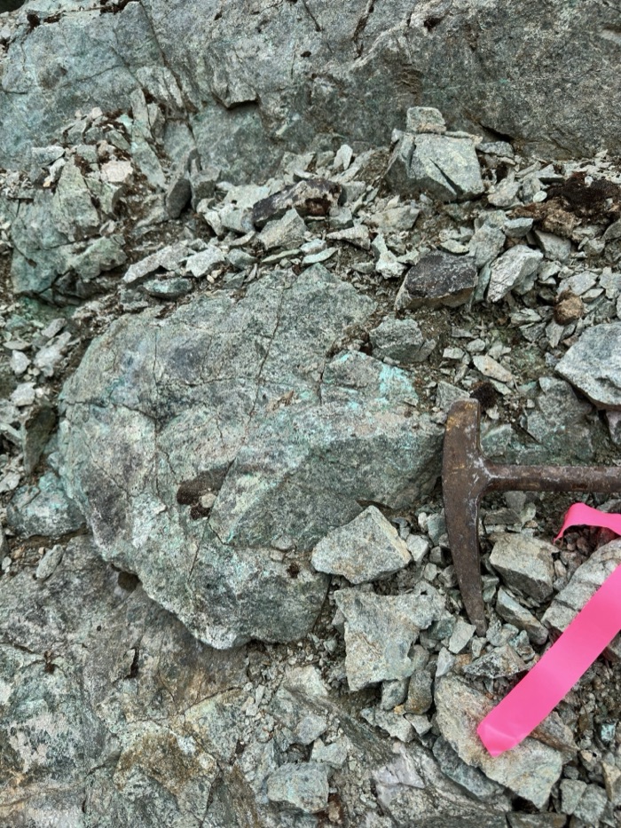 Malachite-stained outcrop with rock hammer for scale
